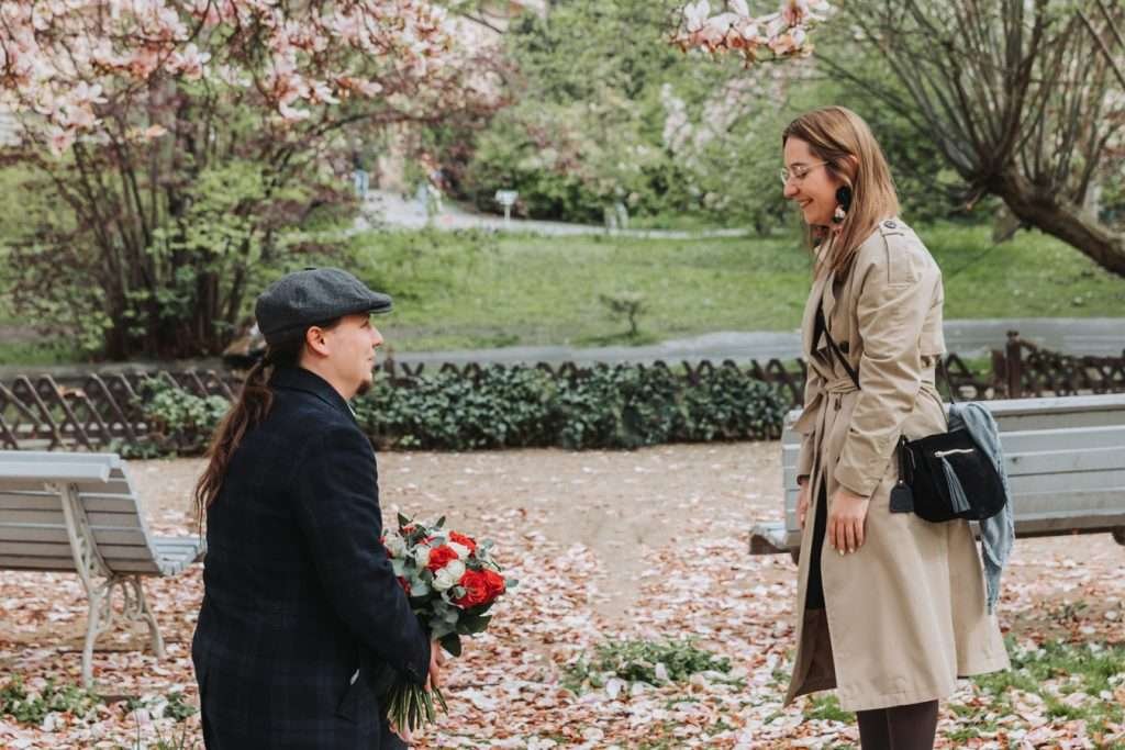 A man holding red and white roses walking towards his partner in a Prague garden in spring